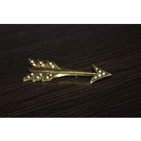 Металлическая брошь со стразами в виде стрелы.