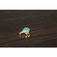 Брошь в виде птицы киви с синими вставками, выполнена в золотом тоне.